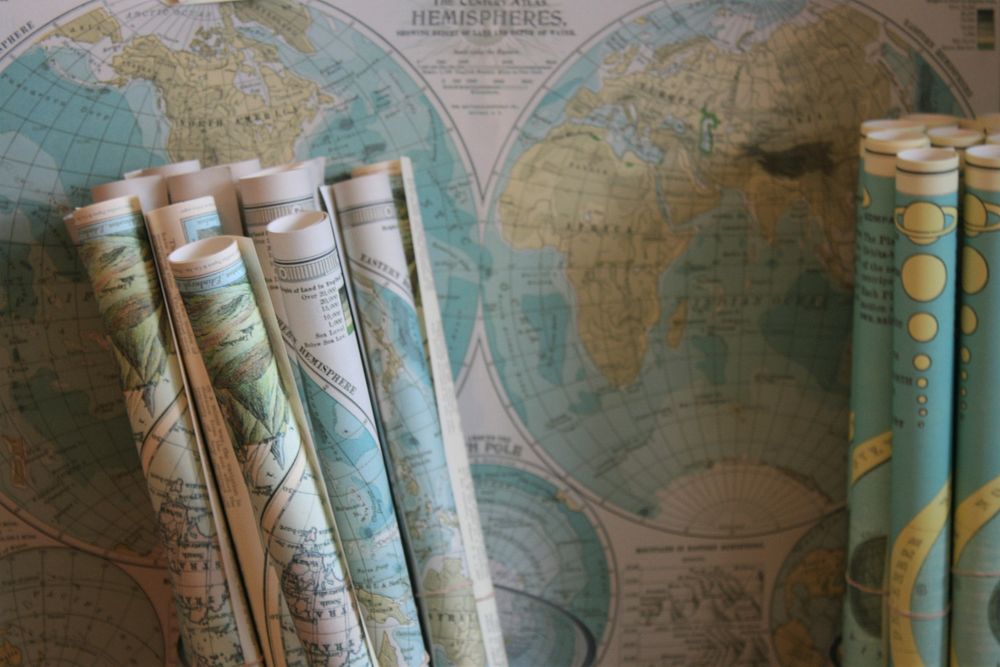 Rolled maps standing against a world map on the wall. Original public domain image from Wikimedia Commons