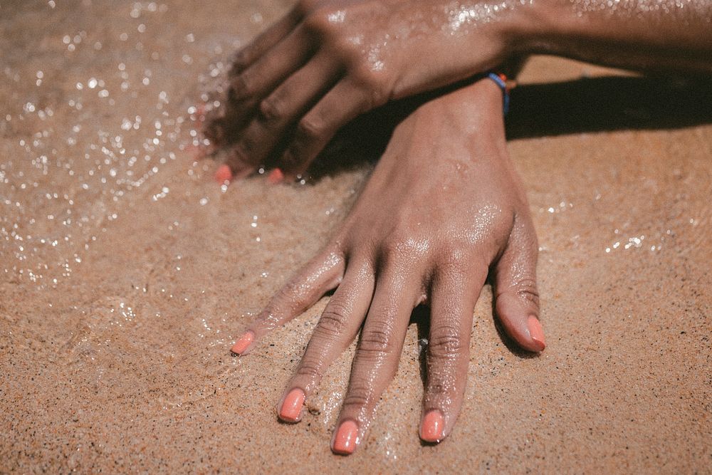 Hands with fingernails painted pink in the wet sand. Original public domain image from Wikimedia Commons