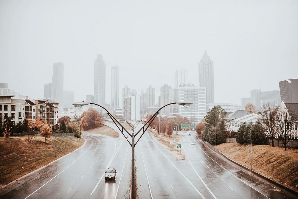 Lone vehicle on a wet highway in Atlanta with fog-covered skyscrapers in the background.. Original public domain image from…