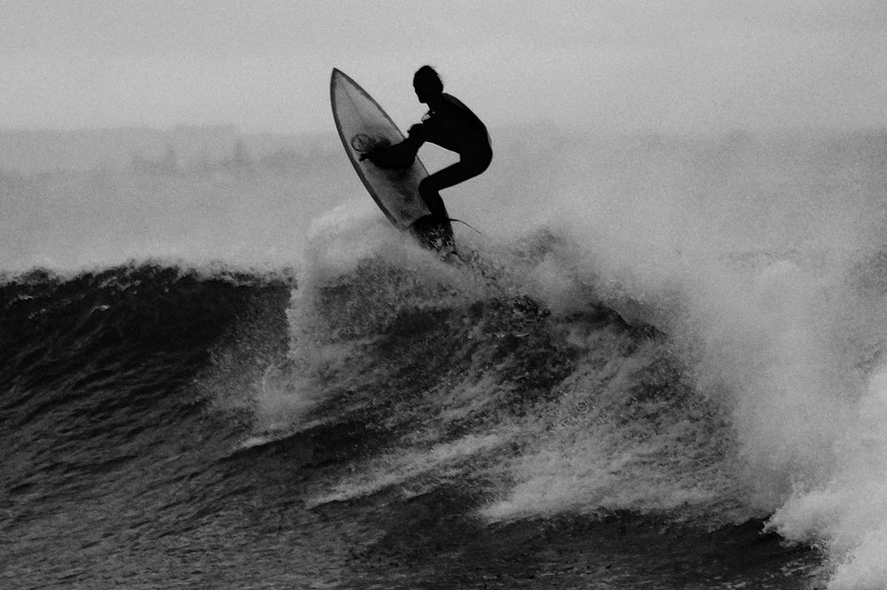 A black and white photo of a surfer catching waves at Point Leo. Original public domain image from Wikimedia Commons