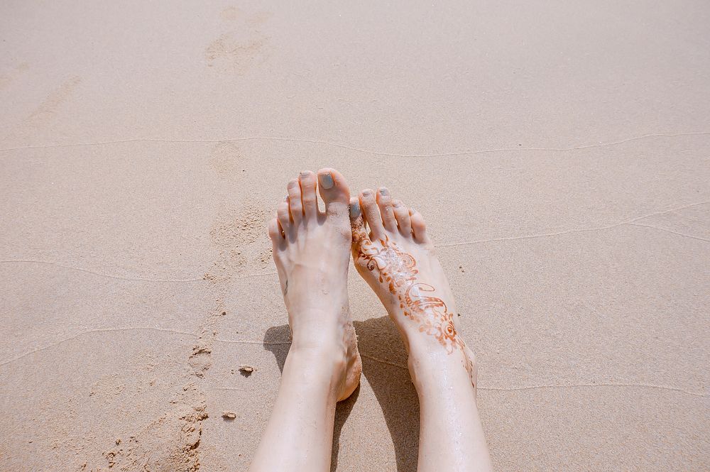 Woman with a henna style tattoo on her foot rests her feet in the sands of El Nido. Original public domain image from…