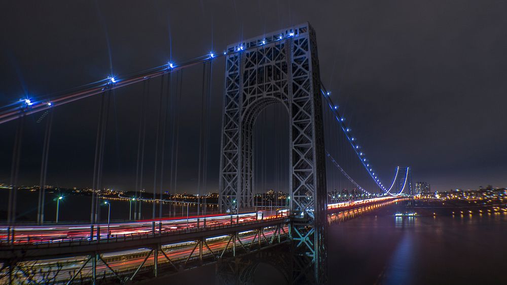 A close-up view of a bridge illuminated with blue lights, taken from the city's skyline. Original public domain image from…