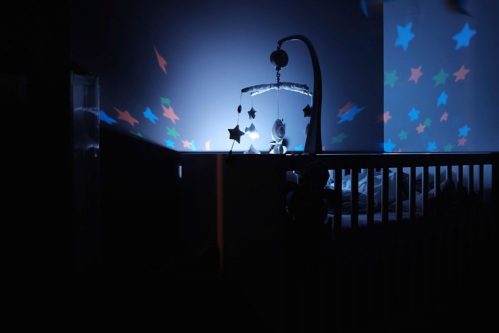 Dark room with a cradle and baby mobile with a night light and stars on the blue walls. Original public domain image from…