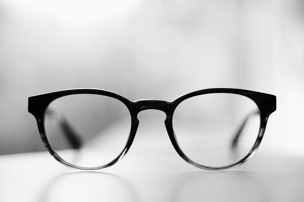 A pair of glasses in black frames on a white surface. Original public domain image from Wikimedia Commons