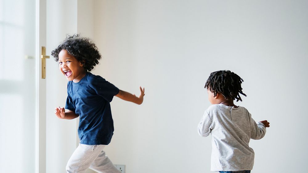 Two black kids playing and chasing each other in an empty room