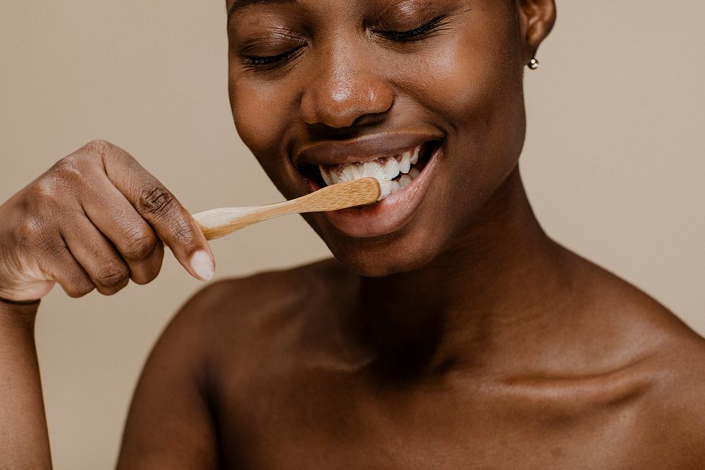 Black woman brushing her teeth with a wooden toothbrush