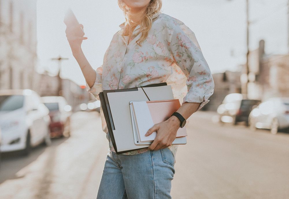 White woman with file folders crossing a street while using her phone