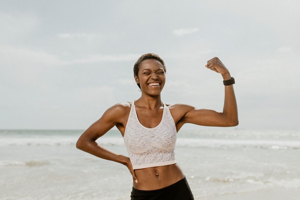 Cheerful black woman flexing her muscles by the seaside