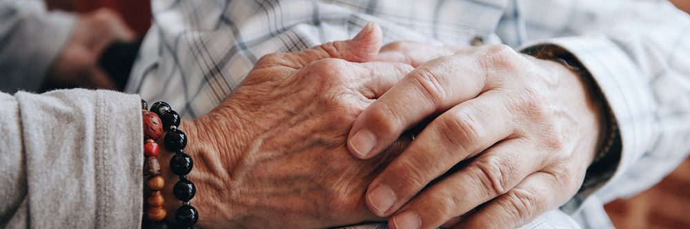 Elderly man on a wheelchair holding his wife hand on his shoulder