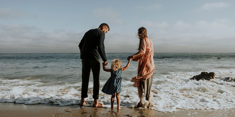 Parents holding daughter's hand at the beach