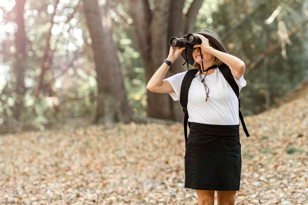 Active retired woman using binoculars to see the beauty of nature