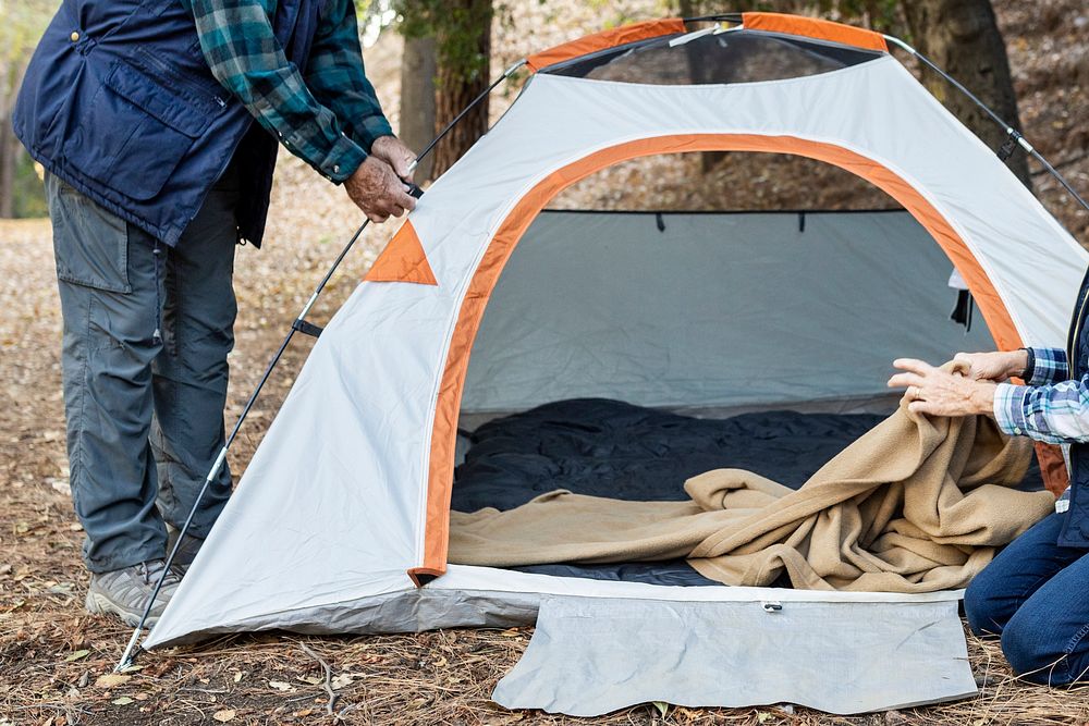 Happy elderly couple setting up a tent in the forest