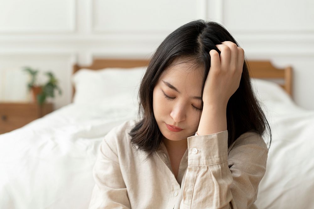 Asian woman sitting sad by her bed