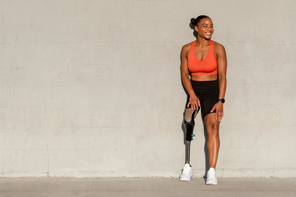 Paralympic athlete with prosthetic leg smiling by the wall