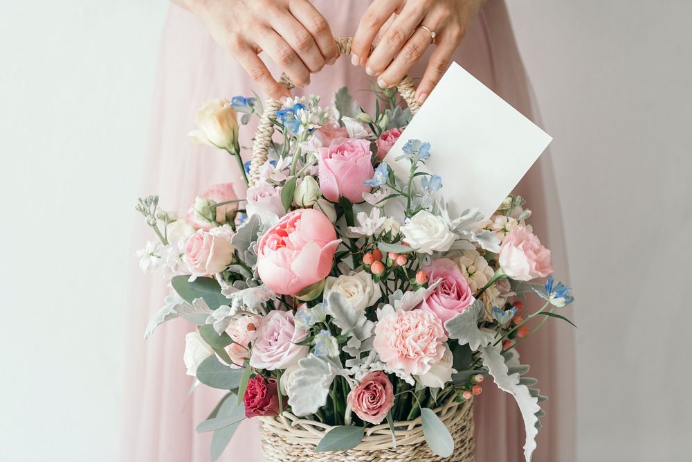 Hand carrying a basket filled with assorted colorful flowers and a note card