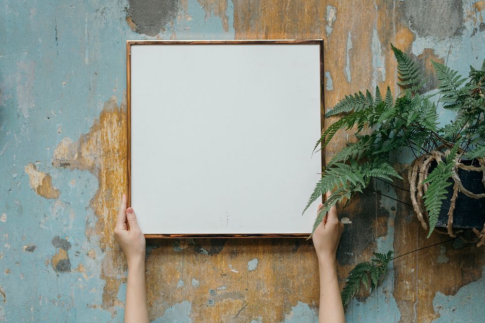 Woman holding a blank frame against a grungy wall