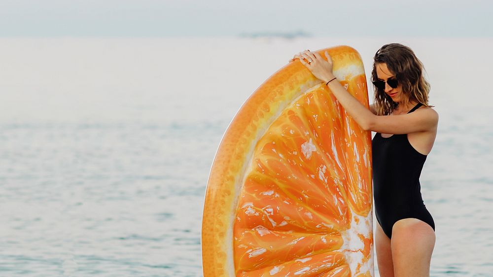 Girl in a black swimsuit with an orange inflatable float at the beach