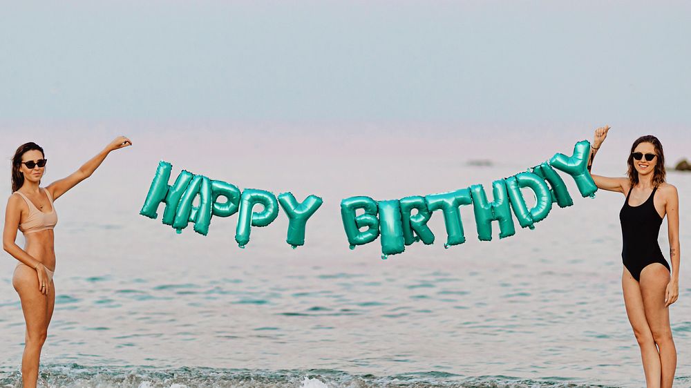 Girls holding a happy birthday foil balloons at the beach