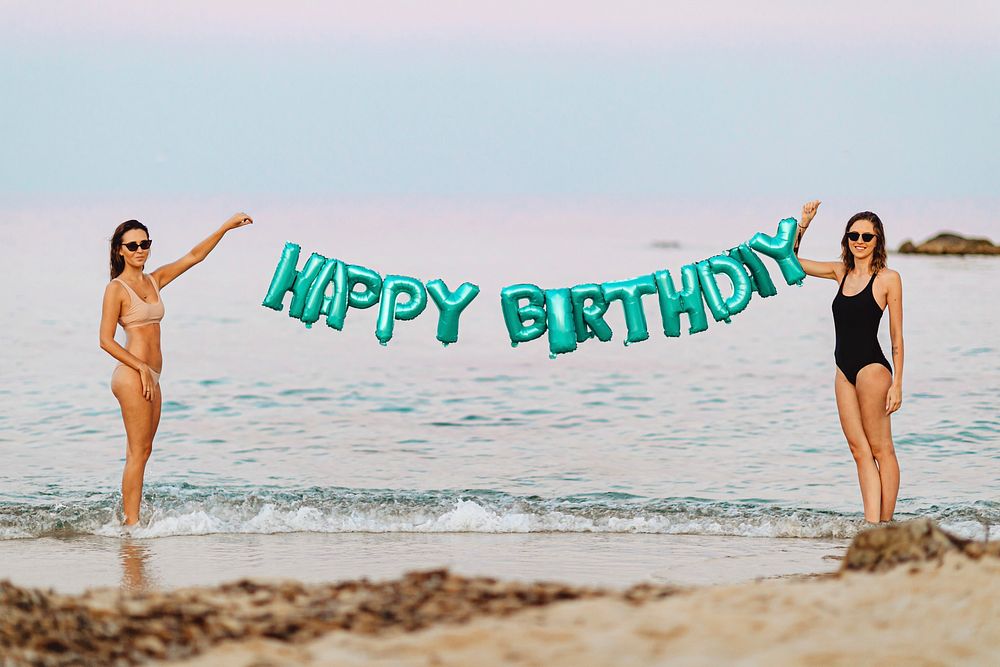 Girls holding a happy birthday foil balloons at the beach