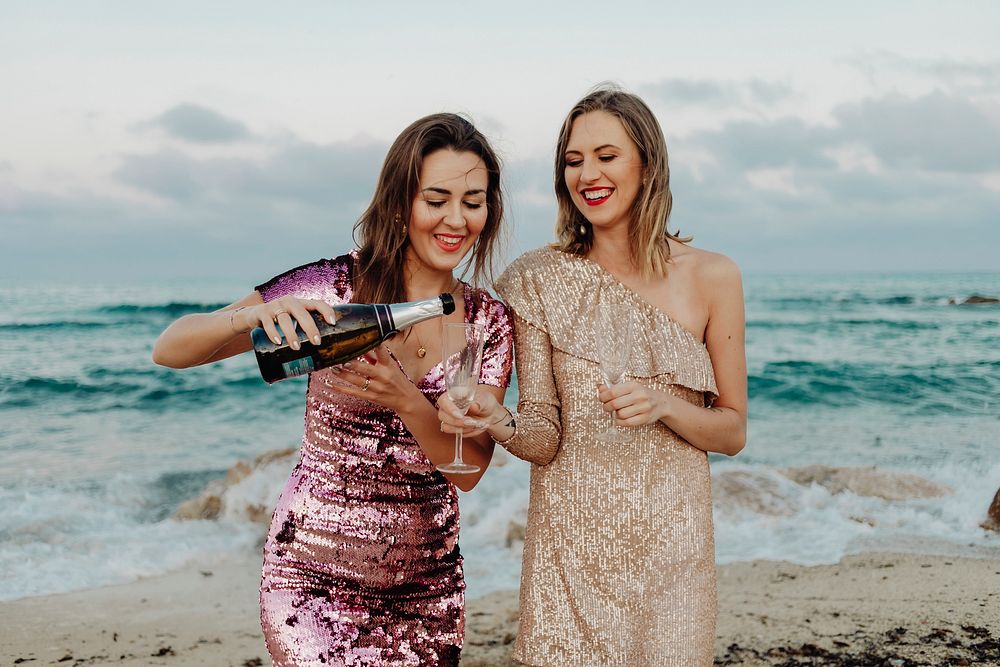 Women filling up a glass of champagne at the beach