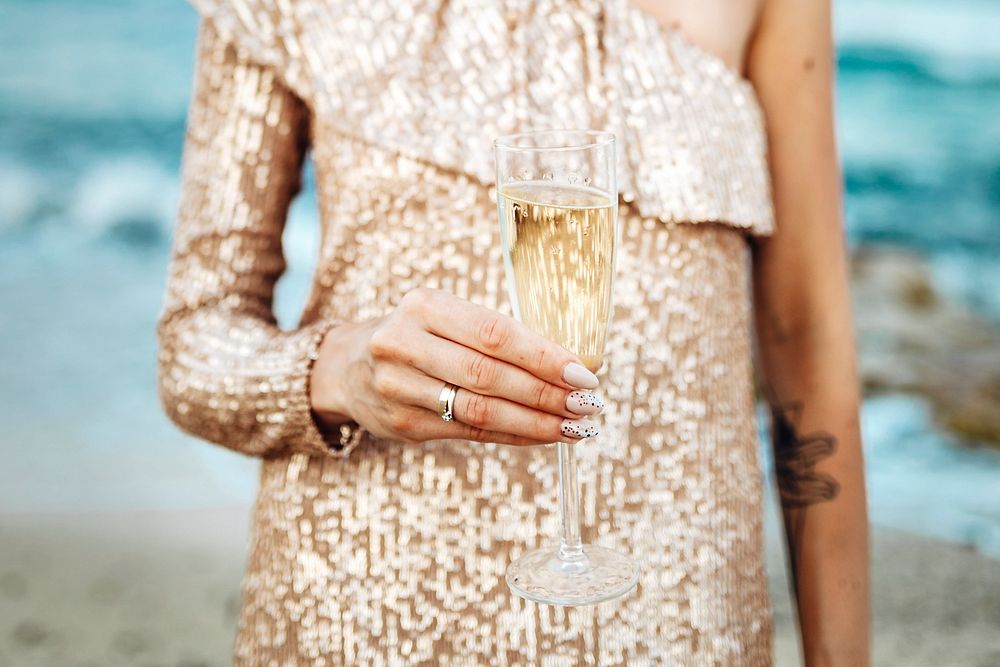 Woman in a gold dress having a glass of champagne at the beach