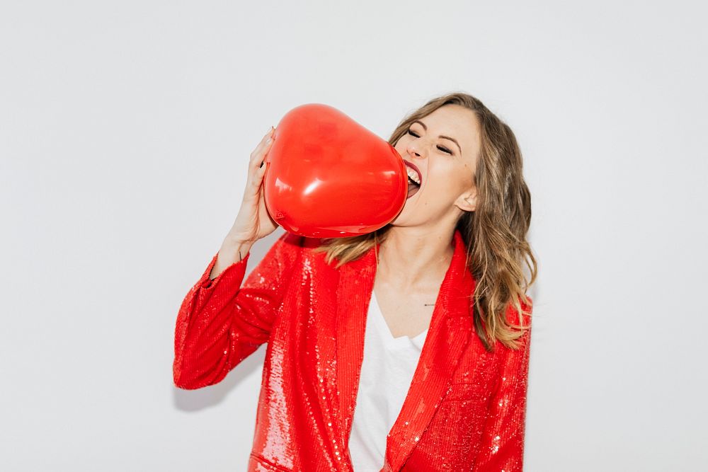 Woman in a red jacket biting a red balloon