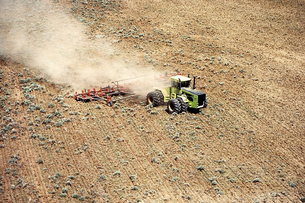 Tractor actively plowing sage and native rangeland to make cropland near Winnett, 1983. Original public domain image from…