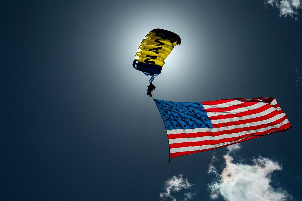 A member of the U.S. Navy Leap Frogs bearing the American flag descends into Frontier Park before the Grand Marshal entrance…