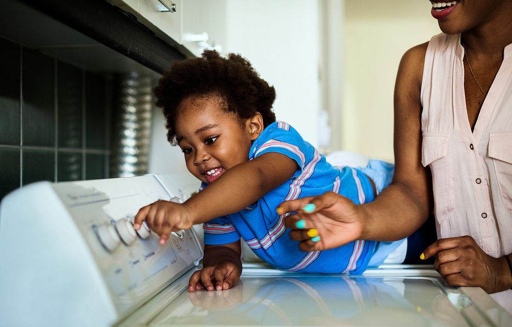 African descent kid helping mom doing the laundry