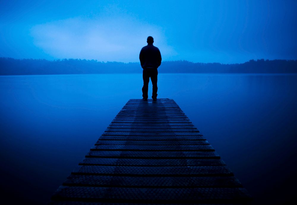 Man standing on a jetty by a tranquil lake.