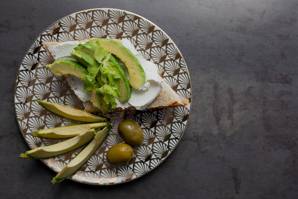 Healthy avocado toast serves on a modern patterned plate with olives flatlay
