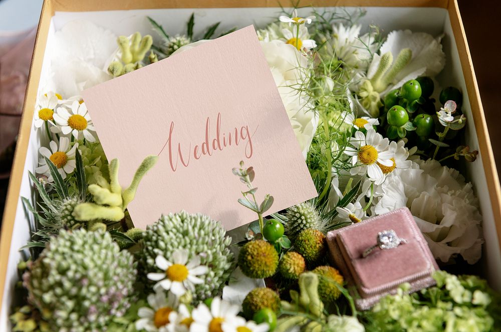 Box filled with various flowers and a wedding ring