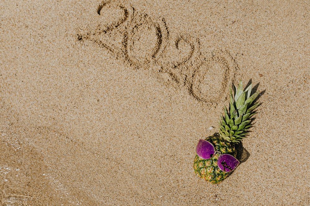Cool pineapple wearing a purple sunglasses with a year 2020 word on the beach