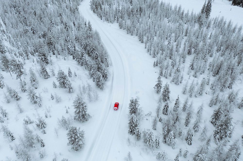 Drone view of a red car driving though a snowy forest in Lapland, Finland