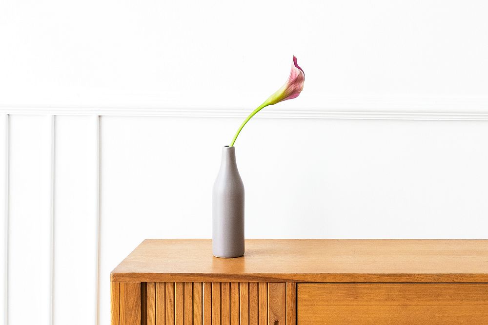 Pink calla lily in a gray vase on a wooden cabinet