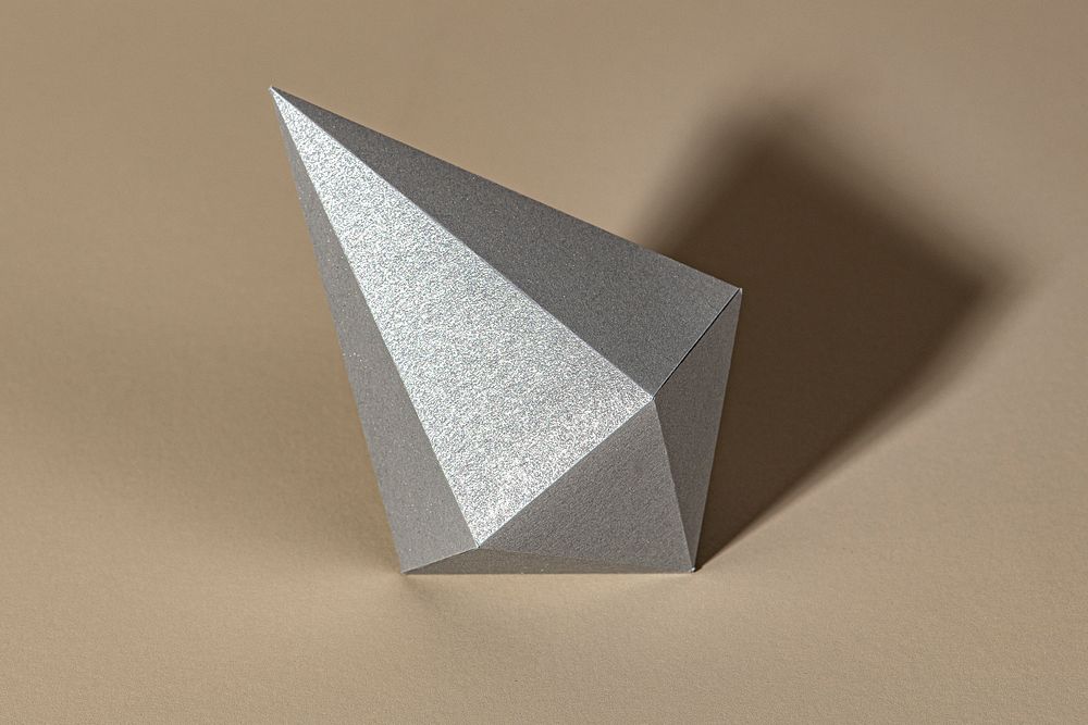 3D silver asymmetric hexagonal bipyramid paper craft on a beige background