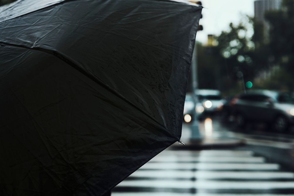 Woman under a black umbrella waiting to cross a street