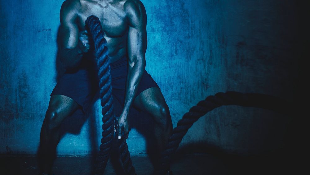 Muscular man doing a battle rope in a gym blue effect