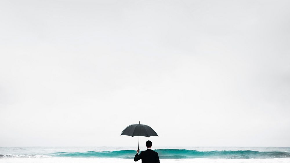 Businessman in suit with umbrella facing sea