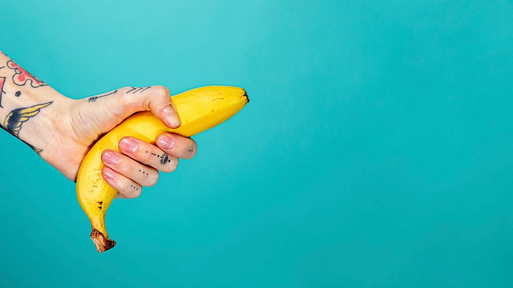 Tattooed hand with a ripe banana on blue background