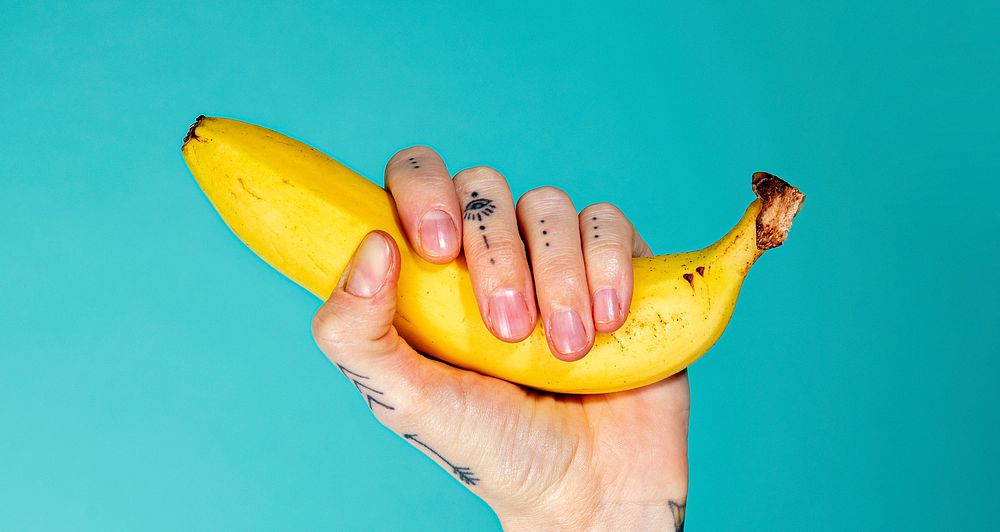 Tattooed hand with a ripe banana on blue background