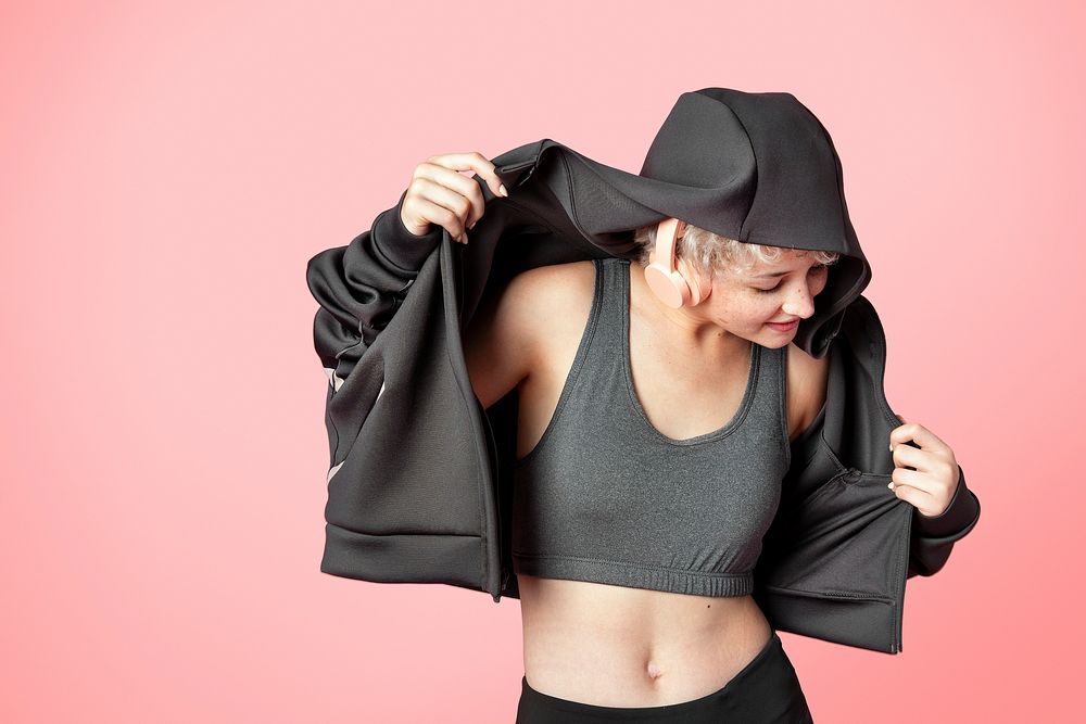 Sporty young girl in a sports bra and a crop hoodie listening to music