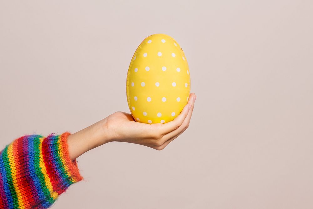 Hand holding a white polka dot patterned yellow egg on a brown background