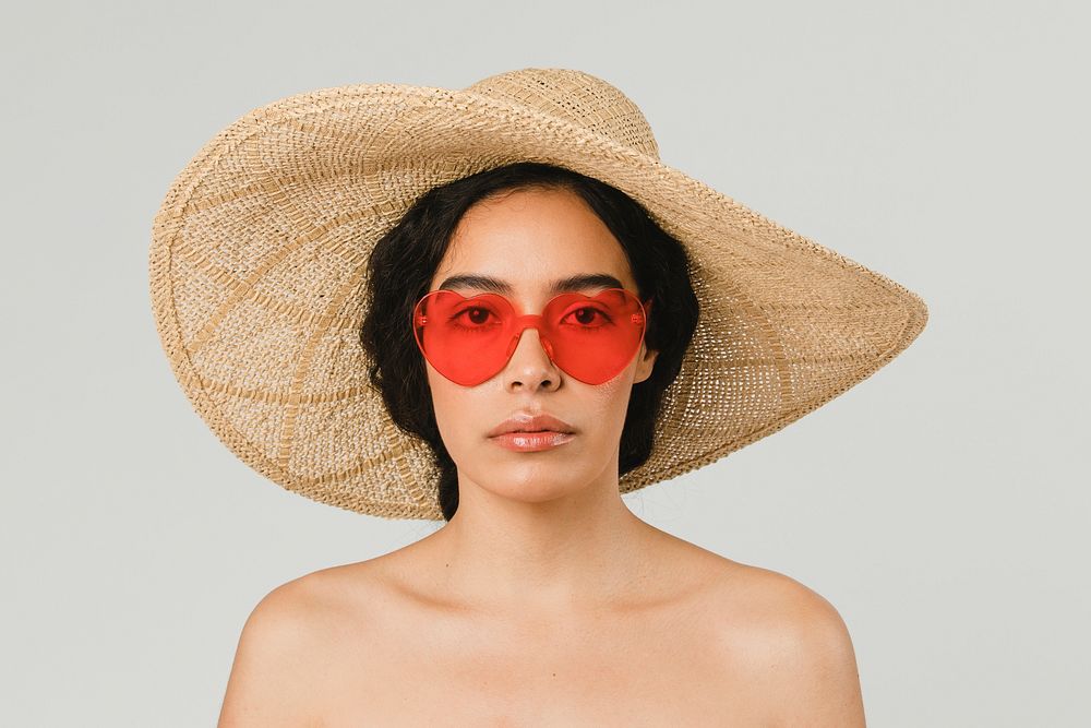 Bare chested woman wearing a big round hat and red vintage heart-shaped sunglasses