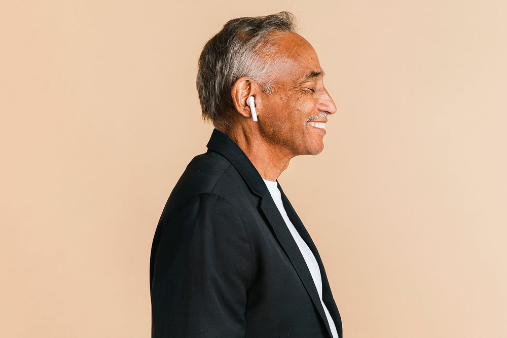 Senior Indian man listening to music with wireless earphones 