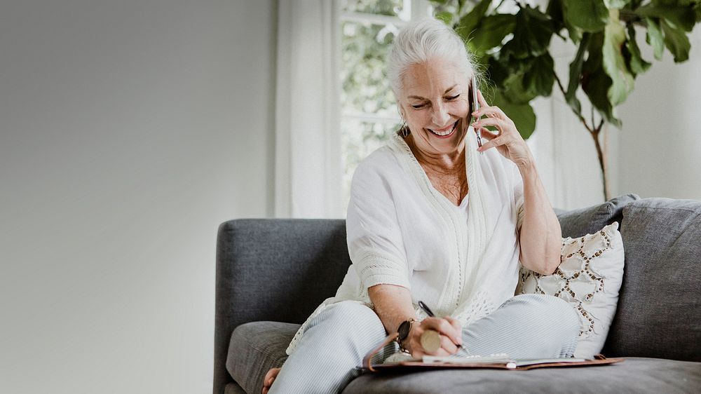 Senior businesswoman on a phone call writing on her planner at home