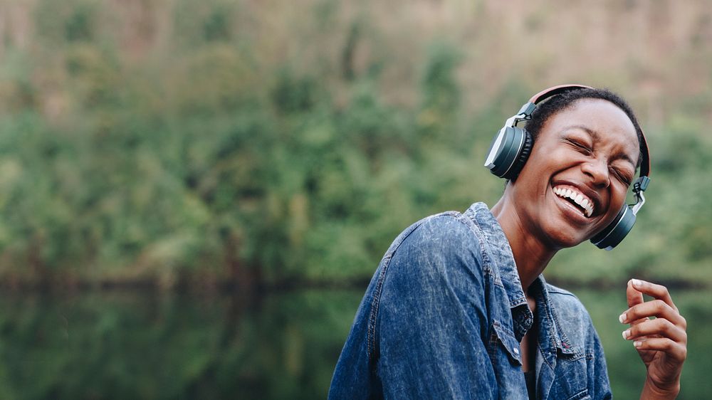 Happy African American woman smiling and enjoying music through her wireless headphones outdoors