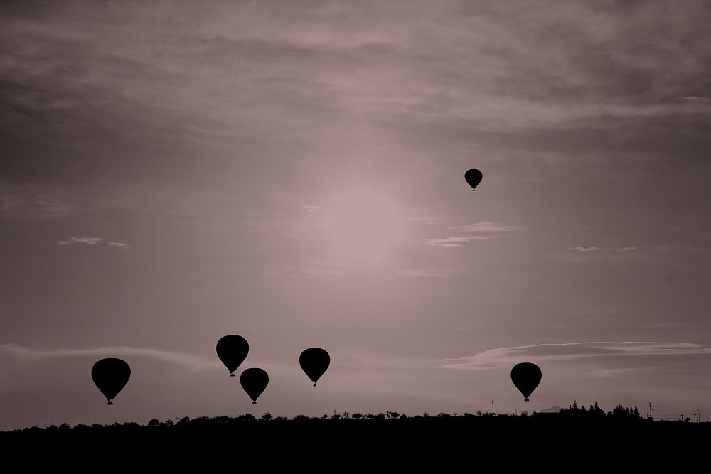 Silhouettes of hot air balloons fly across the sky. Original public domain image from Wikimedia Commons