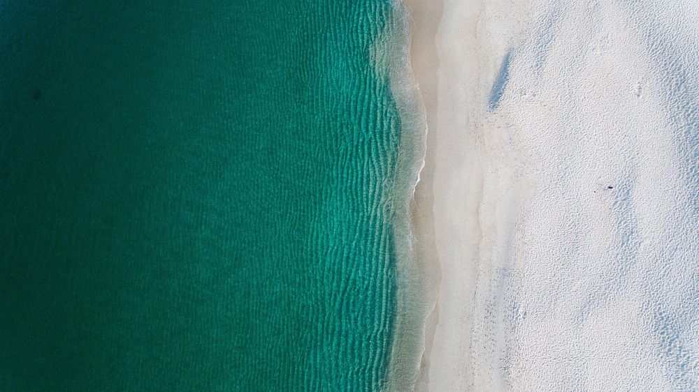 Drone view of a clear ocean washing up on sand shore in Nelson Bay. Original public domain image from Wikimedia Commons
