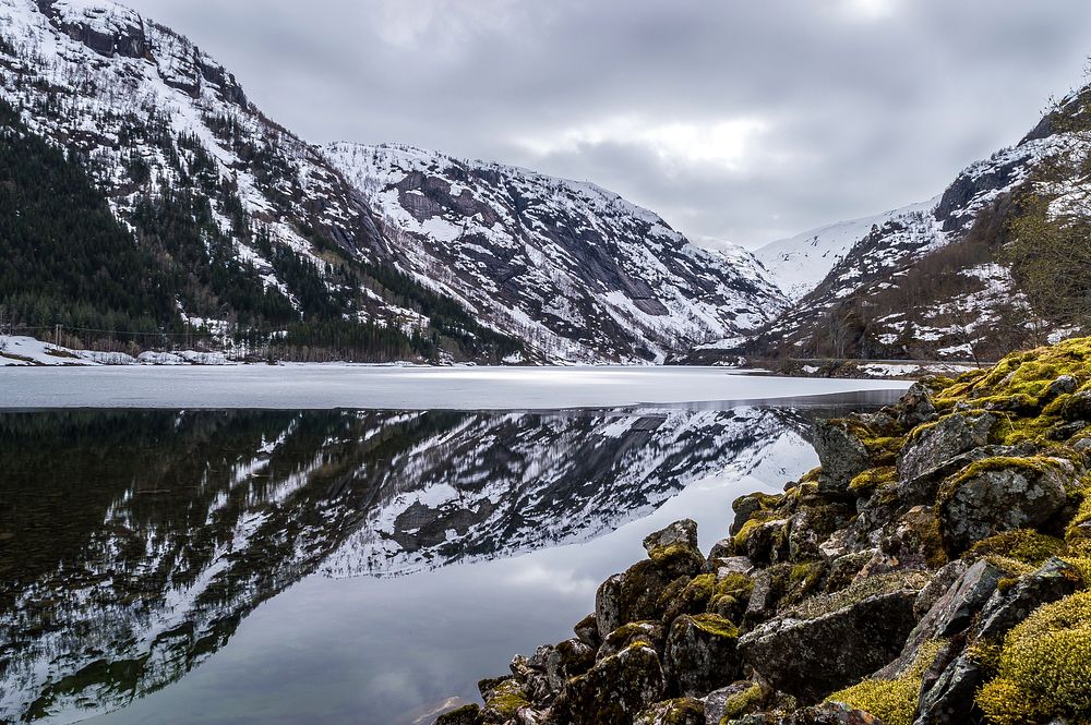 Snowy mountains on a cloudy day reflected in a glassy, melting lake. Original public domain image from Wikimedia Commons